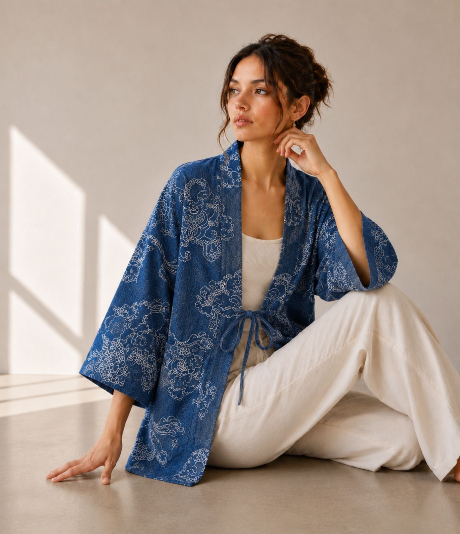 Woman in an indigo denim dragon-print kimono cardigan with tie cords, seated