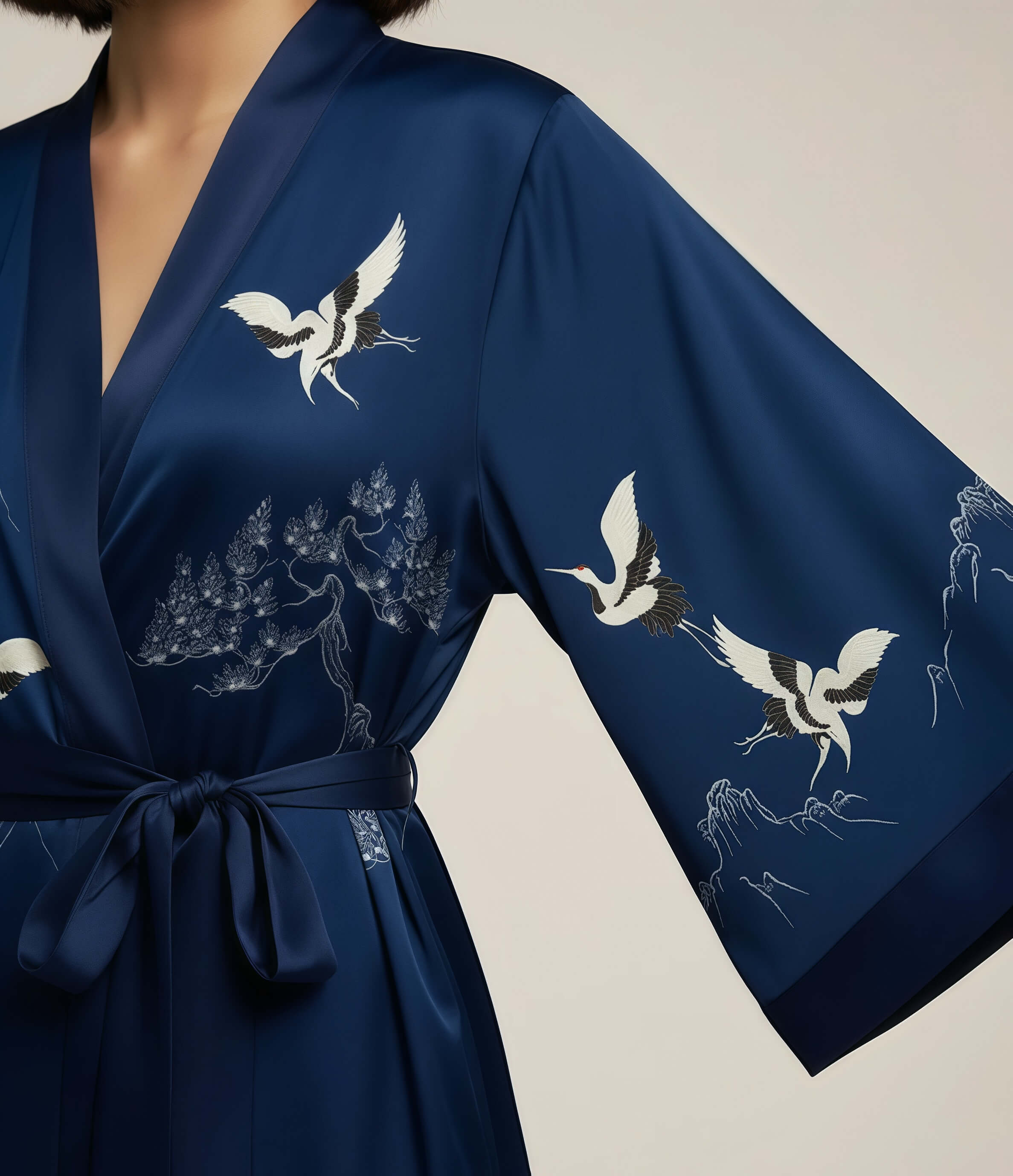 Detail of blue Japanese kimono robe for women featuring white crane print on sleeve and satin fabric with waist belt.