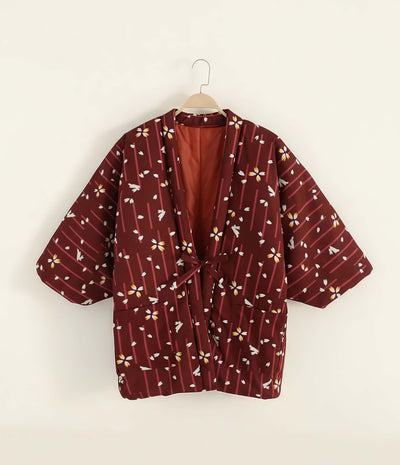 Women’s red Japanese hanten jacket with sakura floral pattern hanging on wooden hanger against neutral background